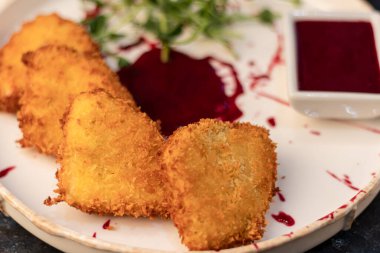 Camembert cheese fried in batter and breadcrumbs with cranberry sauce. Soft and viscous inside. The plate is decorated with a spray of sauce and microgreen. On a wooden background.