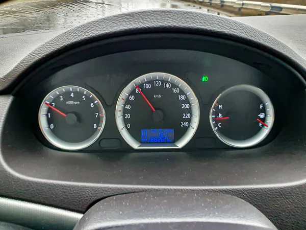 Car dashboard. Speedometer, circular tachometer, oil and fuel level, mileage. Outside the window it is raining, the wipers are visible. — 스톡 사진