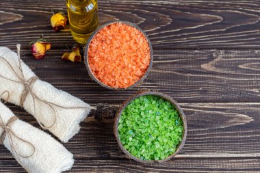 Doğal kokulu deniz, iki renkli banyo tuzu ve banyo havlularıyla spa tedavisi. Arka planda gül yapraklarından yağ var. Ahşap bir arka planda.