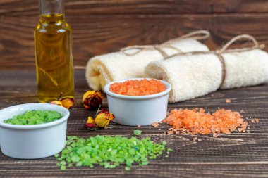 Doğal kokulu deniz, iki renkli banyo tuzu ve banyo havlularıyla spa tedavisi. Arka planda gül yapraklarından yağ var. Ahşap bir arka planda.