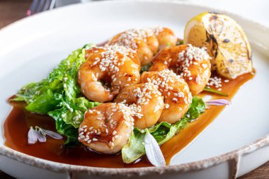 Teriyaki sosunda karides, marul yaprağının üzerinde bir dilim kızarmış limon ile pişirildi. Beyaz arka planda, koyu ahşap bir arka planda..