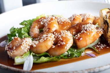 Teriyaki sosunda karides, marul yaprağının üzerinde bir dilim kızarmış limon ile pişirildi. Beyaz arka planda, koyu ahşap bir arka planda..