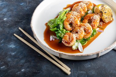 Teriyaki sosunda karides, marul yaprağının üzerinde bir dilim kızarmış limon ile pişirildi. Beyaz arka planda, koyu ahşap bir arka planda..