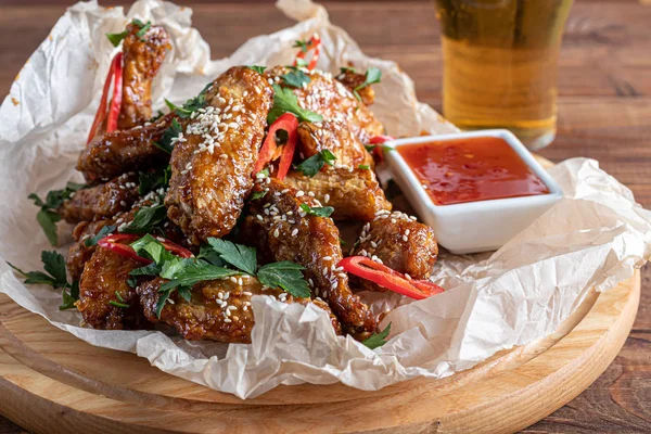 Chicken wings in soy sauce. Served for beer. Sprinkle with sesame seeds. Next to chili pepper sauce and tomatoes. On a wooden board.