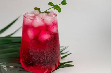 Raspberry-barberry drink in a transparent glass with ice. Added palm branches and raspberries. White background.