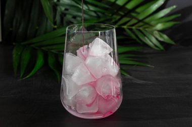 Raspberry-barberry drink in a transparent glass with ice. The drink is poured into a glass. Added palm branches and raspberries. Black background.