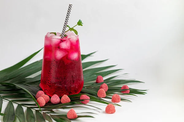 Raspberry-barberry drink in a transparent glass with ice. Added palm branches and raspberries. White background. — Stockfoto