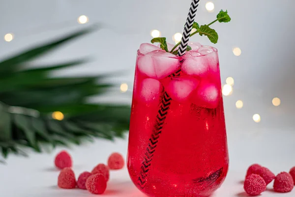 Raspberry-barberry drink in a transparent glass with ice. Added palm branches and raspberries. White background. — Stockfoto