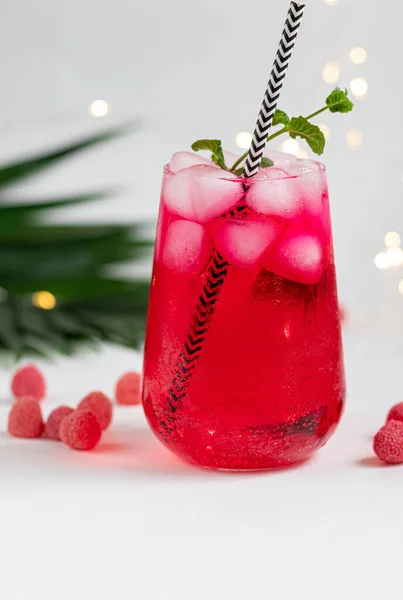 Raspberry-barberry drink in a transparent glass with ice. Added palm branches and raspberries. White background. — Stock Photo, Image