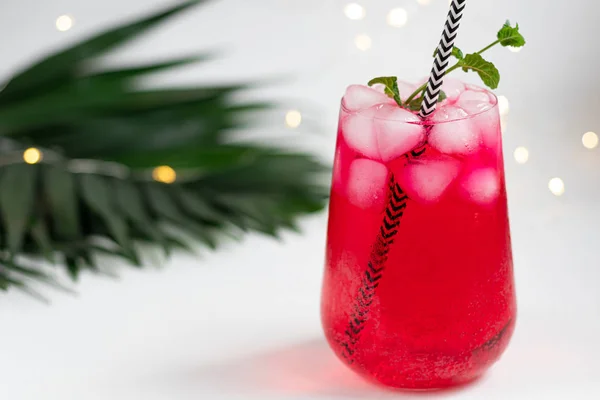 Raspberry-barberry drink in a transparent glass with ice. Added palm branches and raspberries. White background. — Stockfoto