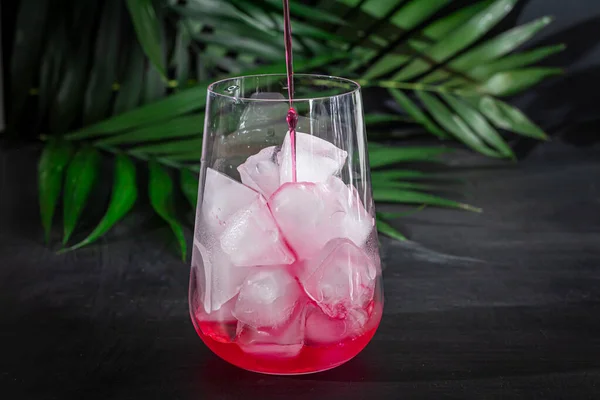 Boisson framboise-épine dans un verre transparent avec glace. La boisson est versée dans un verre. Ajout de branches de palmier et de framboises. Fond noir . — Photo