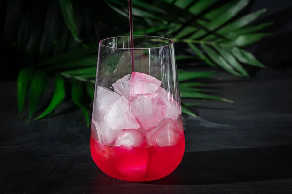 Boisson framboise-épine dans un verre transparent avec glace. La boisson est versée dans un verre. Ajout de branches de palmier et de framboises. Fond noir . — Photo