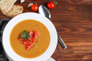 Ahşap zemin üzerinde mercimek olan sebze çorbası. Vişneli domatesle servis edilmiş. Ciabatta parçaları yakınlarda. Arka planda ham büyümeler var. Vejetaryen yemeği. Boşluğu kopyala