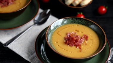 Ahşap arka planda mercimek çorbası. Dilimlenmiş pastırma ve bitkilerle servis edilir. Ciabatta parçaları yakınlarda. Arkaplanda ham iniltiler.