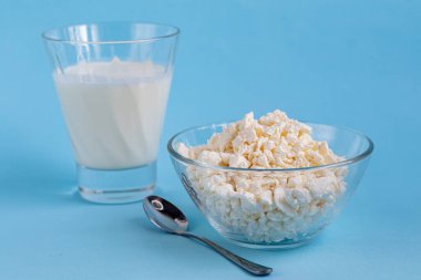 Şeffaf bir kâse içinde taze süzme peynir ve mavi arka planda bir bardak kefir. Mayalanmış yiyecekler. Sağlık için iyi bir bakteri. Boşluğu kopyala