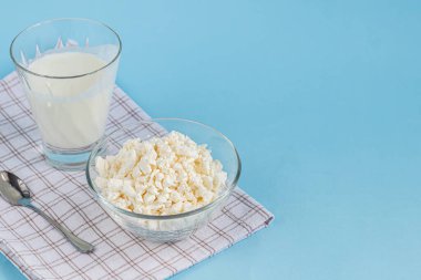 Şeffaf bir kâse içinde taze süzme peynir ve mavi arka planda bir bardak kefir. Mayalanmış yiyecekler. Sağlık için iyi bir bakteri. Boşluğu kopyala