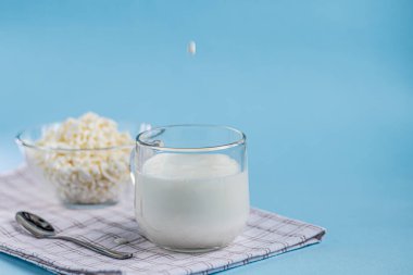 Şeffaf bir kasede şeffaf bir kaşık ve bir bardak kefir akıntısının mavi arka plana döküldüğü taze süzme peynir. Mayalanmış yiyecekler. Sağlık için iyi bir bakteri. Boşluğu kopyala