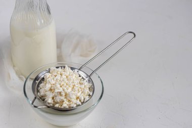 Şeffaf bir kasede kuru üzümlü taze süzme peynir. Arka planda bir bardak kefir var. Mayalanmış yiyecekler. Sağlık için iyi bir bakteri. Hafif arkaplan. Boşluğu kopyala