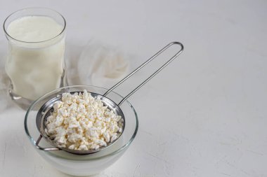 Şeffaf bir kasede kuru üzümlü taze süzme peynir. Arka planda bir bardak kefir var. Mayalanmış yiyecekler. Sağlık için iyi bir bakteri. Hafif arkaplan. Boşluğu kopyala