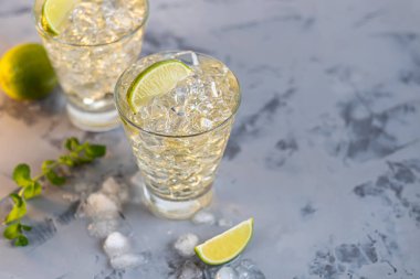 Bardaklar buz ve soğuk yeşil çayla doludur. Limon dilimleri ve bir tutam nane ile süslenmiş. Hafif bir arkaplanda. Boşluğu kopyala