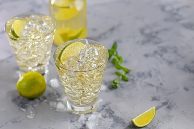 Bardaklar buz ve soğuk yeşil çayla doludur. Limon dilimleri ve bir tutam nane ile süslenmiş. Hafif bir arkaplanda. Boşluğu kopyala