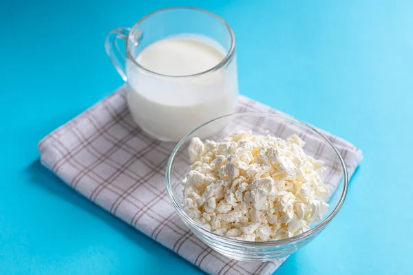 Şeffaf bir kâse içinde taze süzme peynir ve mavi arka planda bir bardak kefir. Mayalanmış yiyecekler. Sağlık için iyi bir bakteri. Boşluğu kopyala