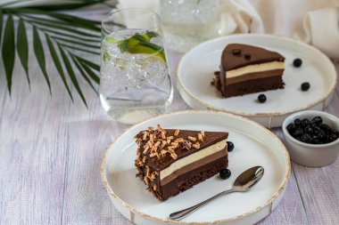 Tatil pastası. Üç çikolata. İki beyaz tabakta iki porsiyon var. Hafif bir arkaplanda. Doğum günü, tatiller, şekerler. Boşluğu kopyala