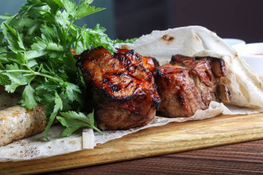 Üzerinde et tabağı olan bir tahta. Tavuk bacağı, kızarmış domuz, sosis, hepsi pide ekmeğinde. Maydanoz. Bardakta ketçaplı hardal. Karanlık bir arka planda. Boşluğu kopyala