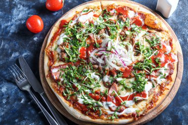 Domuz pastırmalı pizza ve ahşap bir tabakta peynir ve domates soslu otlar. Karanlık bir arka planda. Boşluğu kopyala