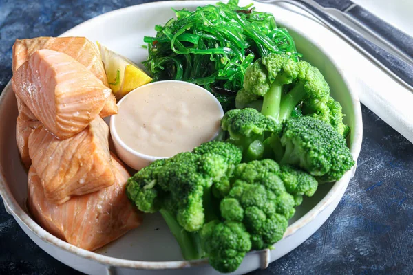 Steamed salmon with broccoli and seaweed salad. Diet healthy eating. On a dark background. Copy space