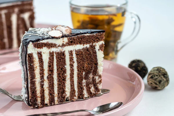 A slice of Zebra cake with chocolate icing. On a light background. In the background is a cup with floral tea. Copy space