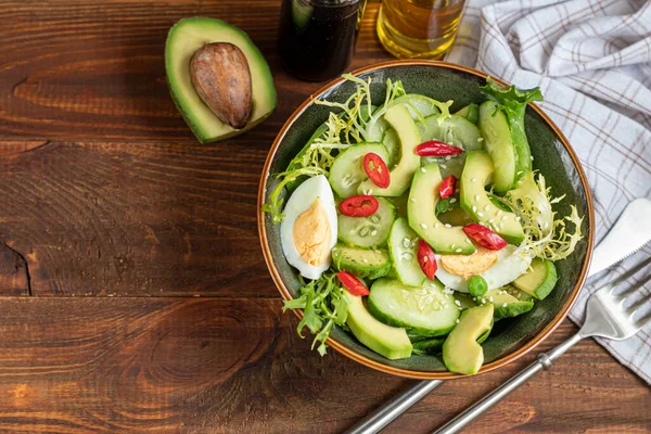 Taze salatalık, ıspanak yaprağı, roka, avokado. Dilimlenmiş yumurta ve kırmızı biberle servis ediliyor. Beslenme düzeni. Tüm aile için bir kahvaltı. Vitamin tabağı. Koyu ahşap bir arka planda. Boşluğu kopyala