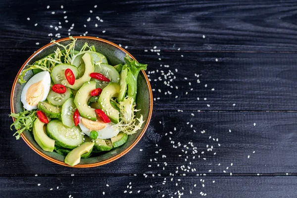 Taze salatalık, ıspanak yaprağı, roka, avokado. Dilimlenmiş yumurta ve kırmızı biberle servis ediliyor. Beslenme düzeni. Tüm aile için bir kahvaltı. Vitamin tabağı. Koyu ahşap bir arka planda. Boşluğu kopyala