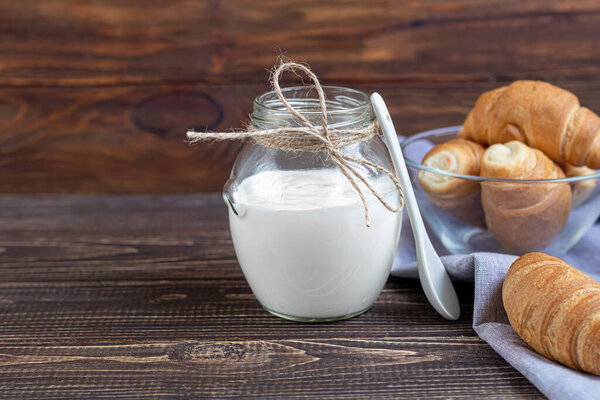 Homemade yogurt in a glass jar on a wooden light background with a ceramic spoon. Healthy diet food. Vegetarian food. Copy space