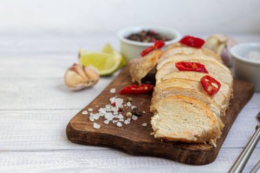 Fırında pişirilmiş tavuk göğsü, tahta bir tahtada dilimlenmiş. Kırmızı biberle servis edilmiş. Yakınlarda sarımsak, kaba tuz, limon ve biber var. Beslenme düzeni. Boşluğu kopyala