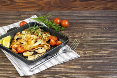 Fırında ızgarada karnabahar bifteği. Yakınlarda vişneli domatesler, bir tutam nane, limon ve biber var. Beslenme düzeni. Vejetaryenlik. Koyu bir ahşap arka planda.