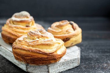 Kuru üzüm ve kuru meyveli fırın ürünleri koyu ahşap arka planda yer almaktadır. Üzerine krema serpilmiş şeker. Kraffinler. Paskalya yemeği. Boşluğu kopyala