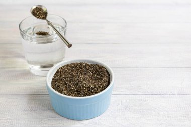 Cam bir kasede siyah chia tohumları ve içinde ıslandıkları su. Metal kaşıkla beyaz bir arka planda. Boşluğu kopyala.