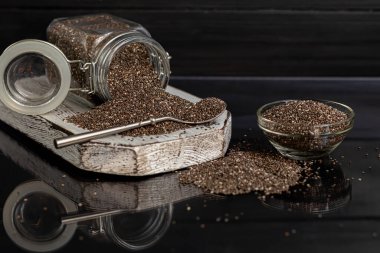 Cam kaplamalı siyah chia tohumları sağlıklı vitamin ve mineraller içerir. Metal kaşıkla siyah bir arka planda. Boşluğu kopyala