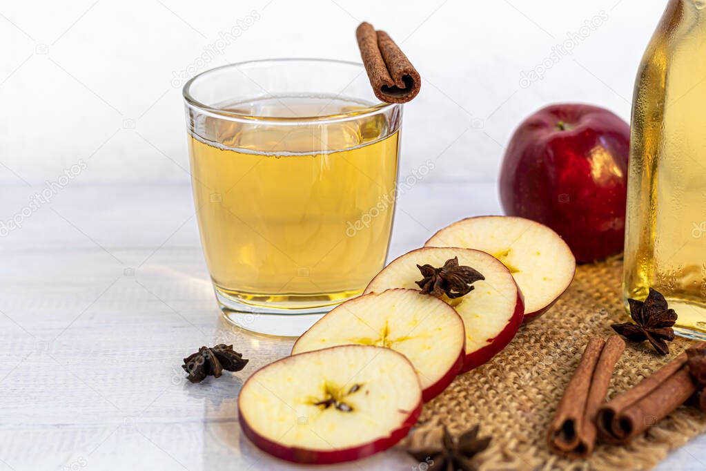 Healthy organic foods. Apple cider in a glass bowl and fresh red apples on a light background. In a glass of ice cubes and nearby cinnamon sticks. Copy space