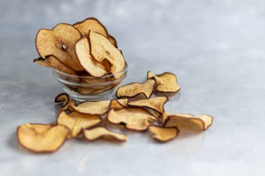 Gri arka planda çıtır armut cipsi. Arka planda olgun armutlar var. Sağlıklı yemek, dekor. Boşluğu kopyala