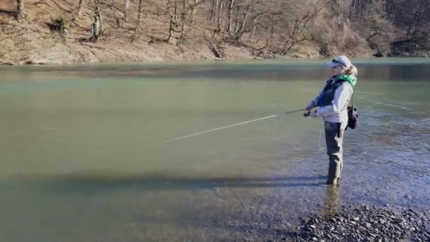 Eine Frau fängt einen rotierenden Fisch, während sie am Ufer des Flusses steht — Stockvideo