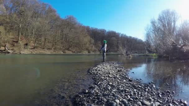 Женщина ловит крутящуюся рыбу стоя на берегу реки — стоковое видео