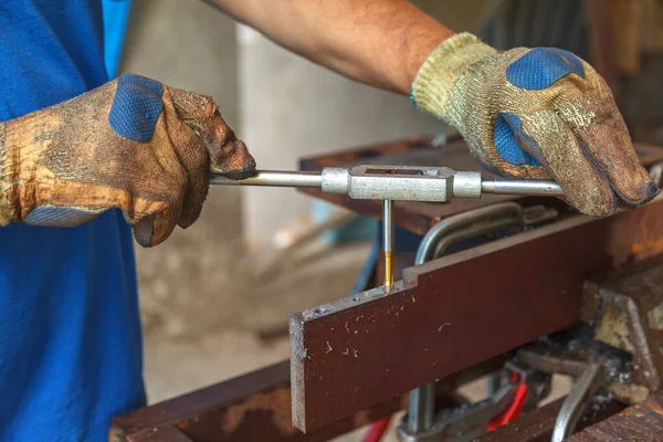 Sarı ve mavi koruyucu eldivenli işçiler el dokunuşuyla iç ipliği kestiler. Metal bir ürünün elle bağlanma kullanılarak hazırlanması