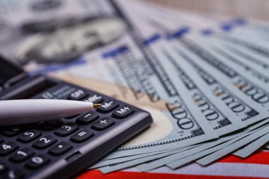 Hesap makinesinin üzerinde duran dolarlar üzerine kurulu bir kalem, yakın plan. Başarılı finansal iş kavramı. Yan üst görünüm