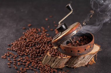 Taze kavrulmuş, buharda pişmiş kahve taneleri eski bir el yapımı fasulye kızartma aletinde. Ahşap bir stantta dumanlı kavrulmuş kahve. Yan üst görünüm.
