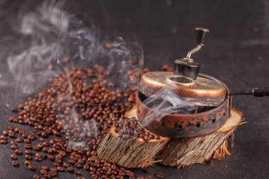Taze kavrulmuş, buharda pişmiş kahve taneleri eski bir el yapımı fasulye kızartma aletinde. Ahşap bir stantta dumanlı kavrulmuş kahve. Yan üst görünüm.