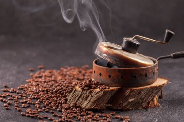 Taze kavrulmuş, buharda pişmiş kahve taneleri eski bir el yapımı fasulye kızartma aletinde. Ahşap bir stantta dumanlı kavrulmuş kahve. Yan üst görünüm.