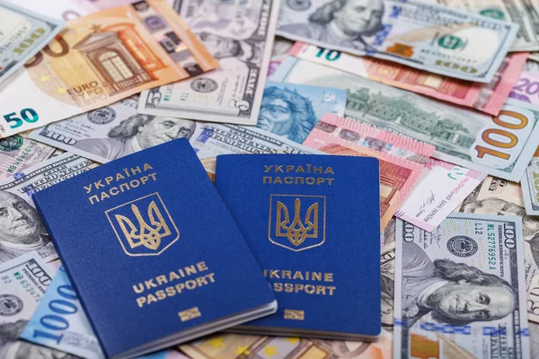 İki Ukrayna biyometrik pasaportu, dünyanın farklı ülkelerinden gelen para birimlerinin arka planına, avro, dolar, hryvnias, forints 'e karşı yalan söylüyor. Yurtdışında turizm ve eğlence kavramı. Üst taraf görünümü.