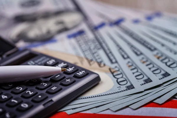 Hesap makinesinin üzerinde duran dolarlar üzerine kurulu bir kalem, yakın plan. Başarılı finansal iş kavramı. Yan üst görünüm